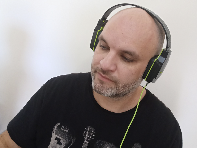Homem pardo careca com barba branca, usando um headpone com uma blusa preta